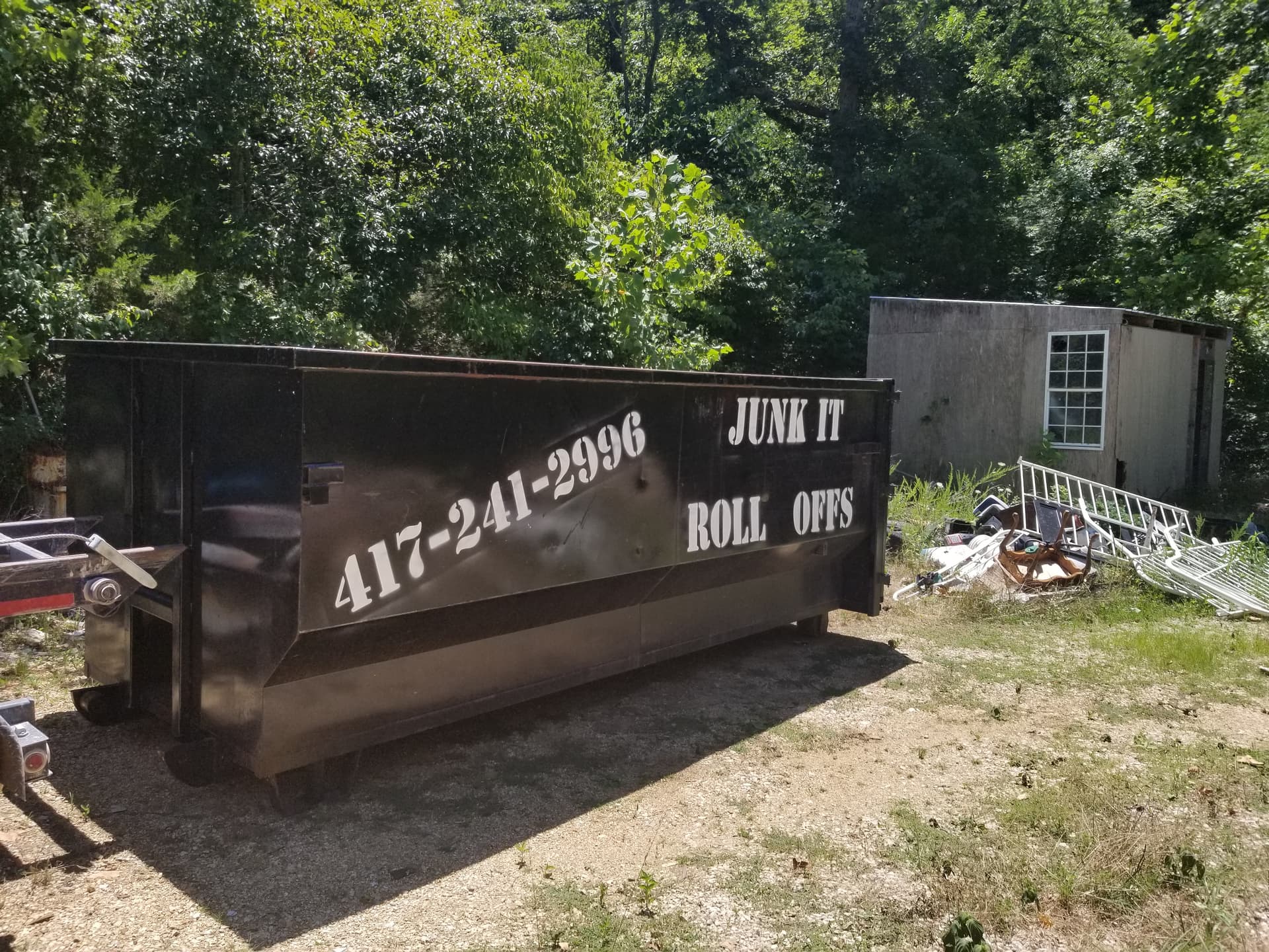 Black 25-yard roll-off dumpster from Junk It Roll Offs in a rural setting in Ava, MO, used for a general property cleanout next to a shed.