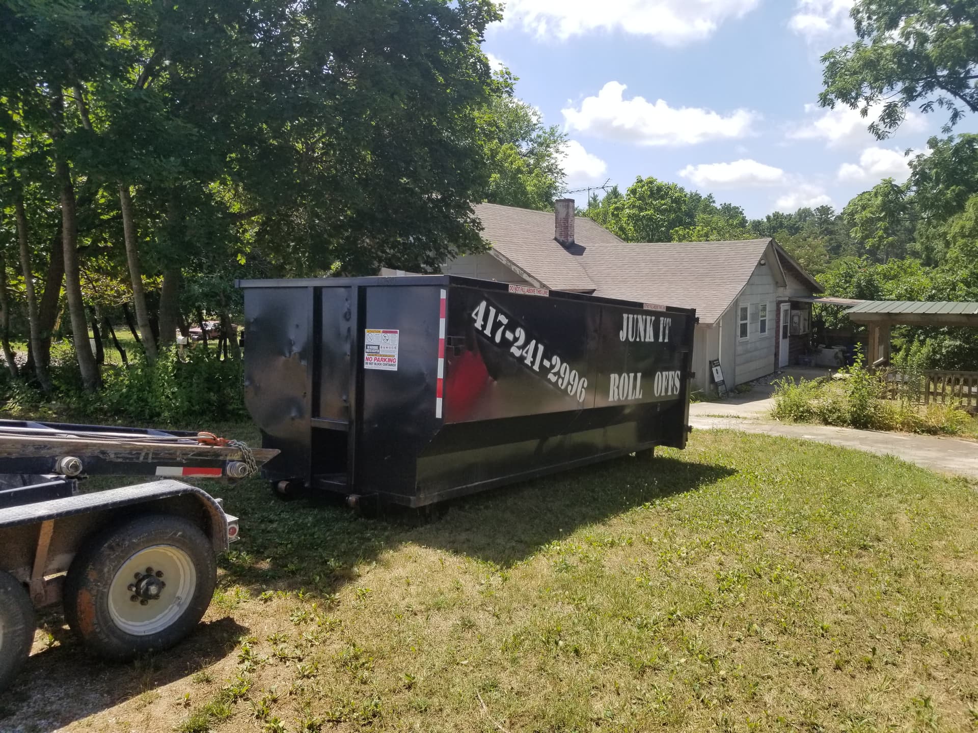 Black 25-yard roll-off dumpster from Junk It Roll Offs on a trailer in a residential yard in Seymour, MO.